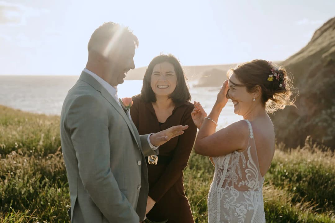 Bride touching her face beside the groom and celebrant at a seaside ceremony.