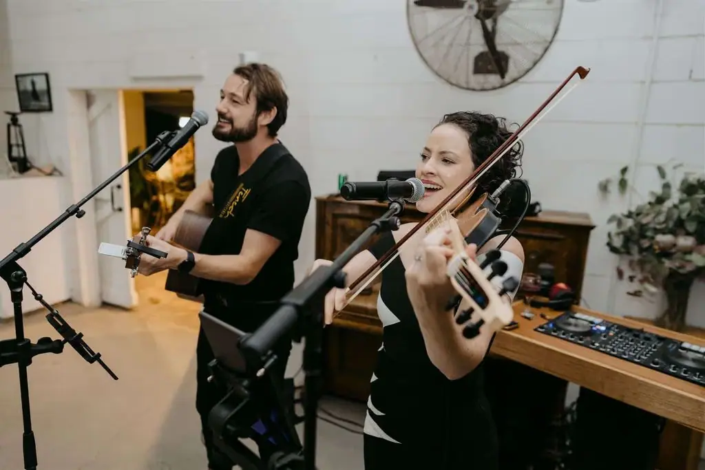Guitarist and violinist performing together with microphones indoors.