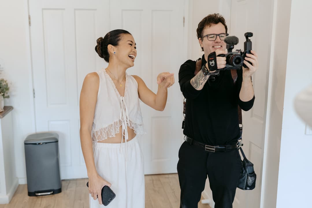 Woman laughing beside a camera operator filming indoors.
