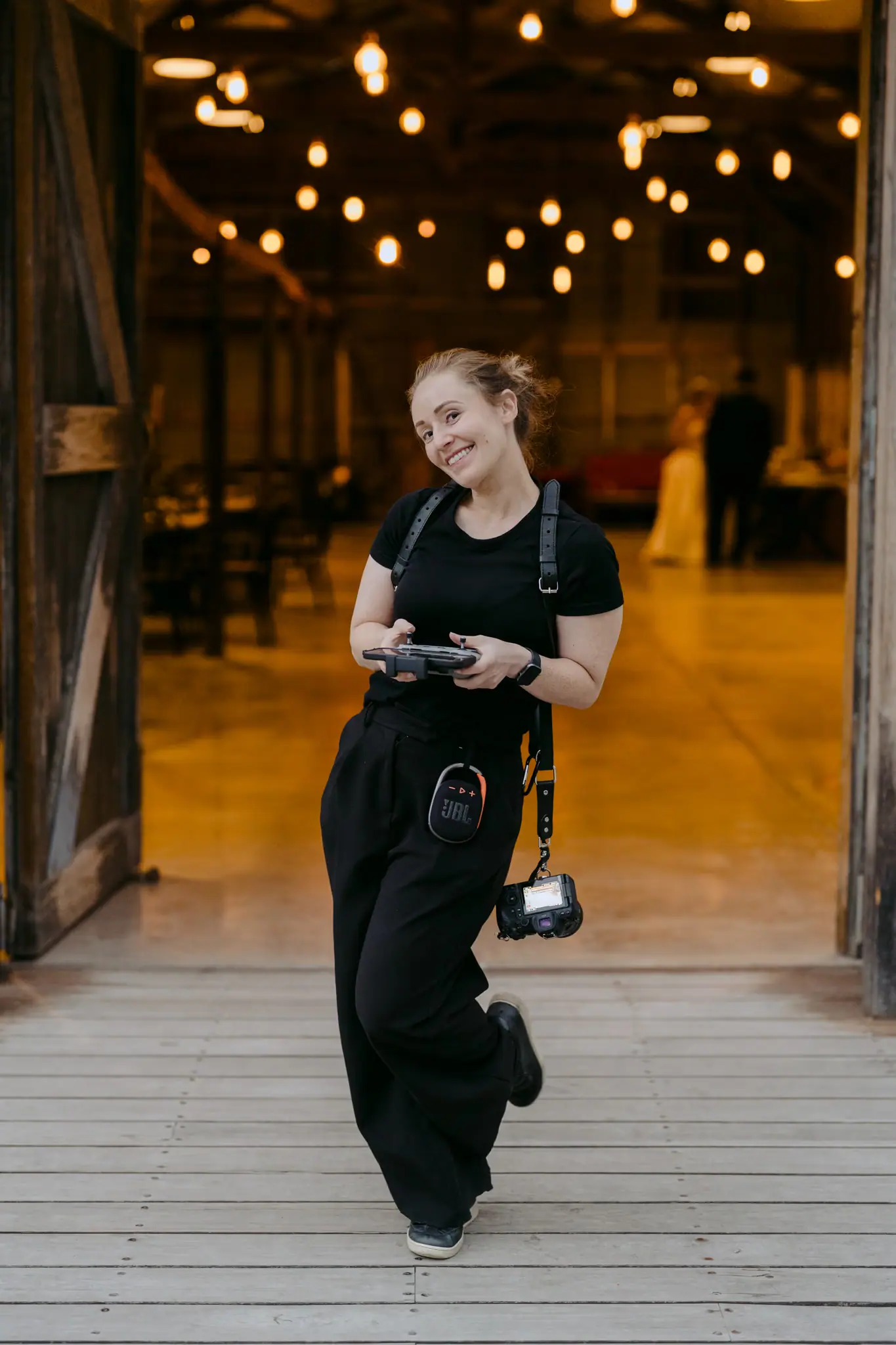 Camera-carrying woman smiling as she walks out of a lit reception doorway.