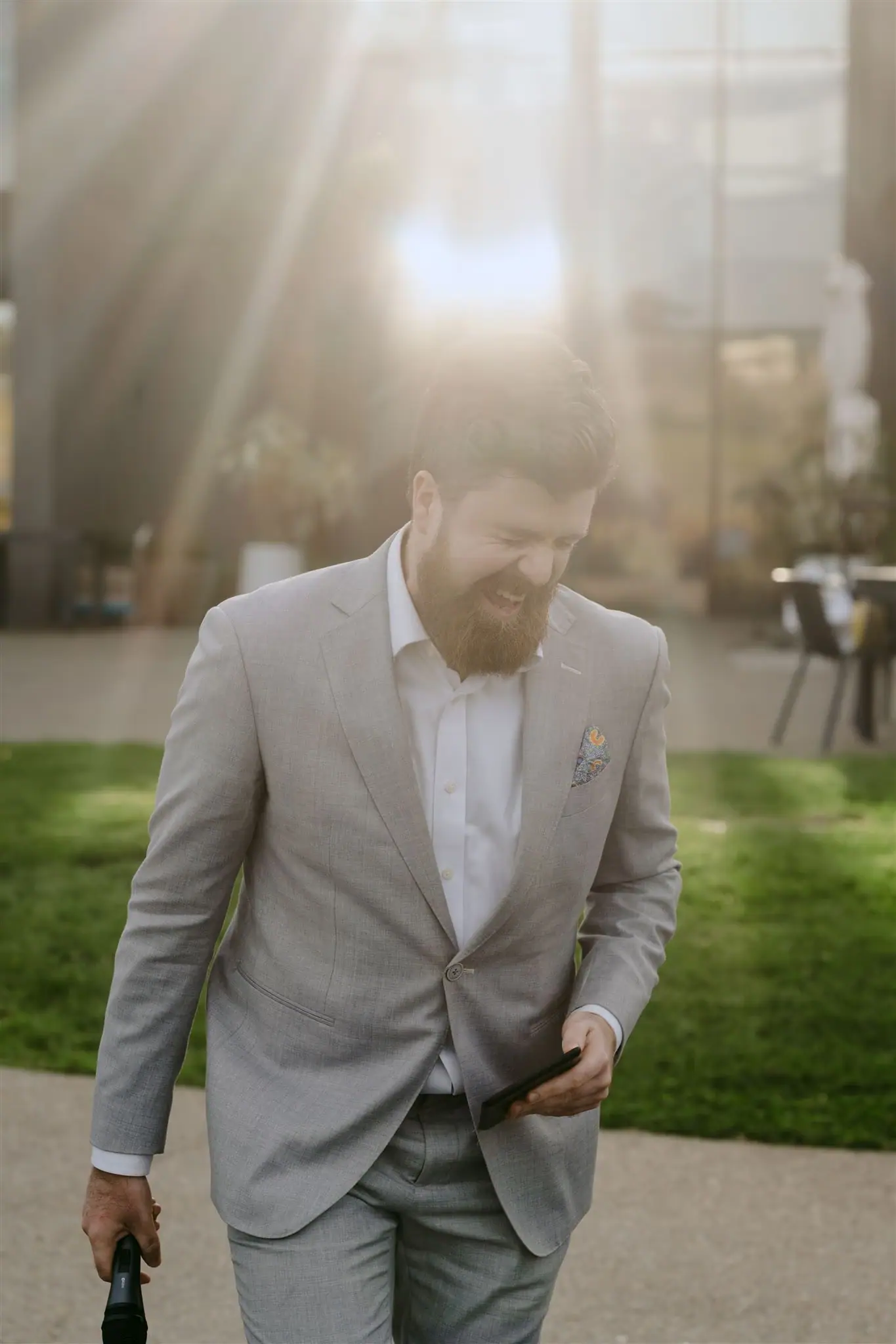 Man in a pale suit walking through a garden in bright backlighting.