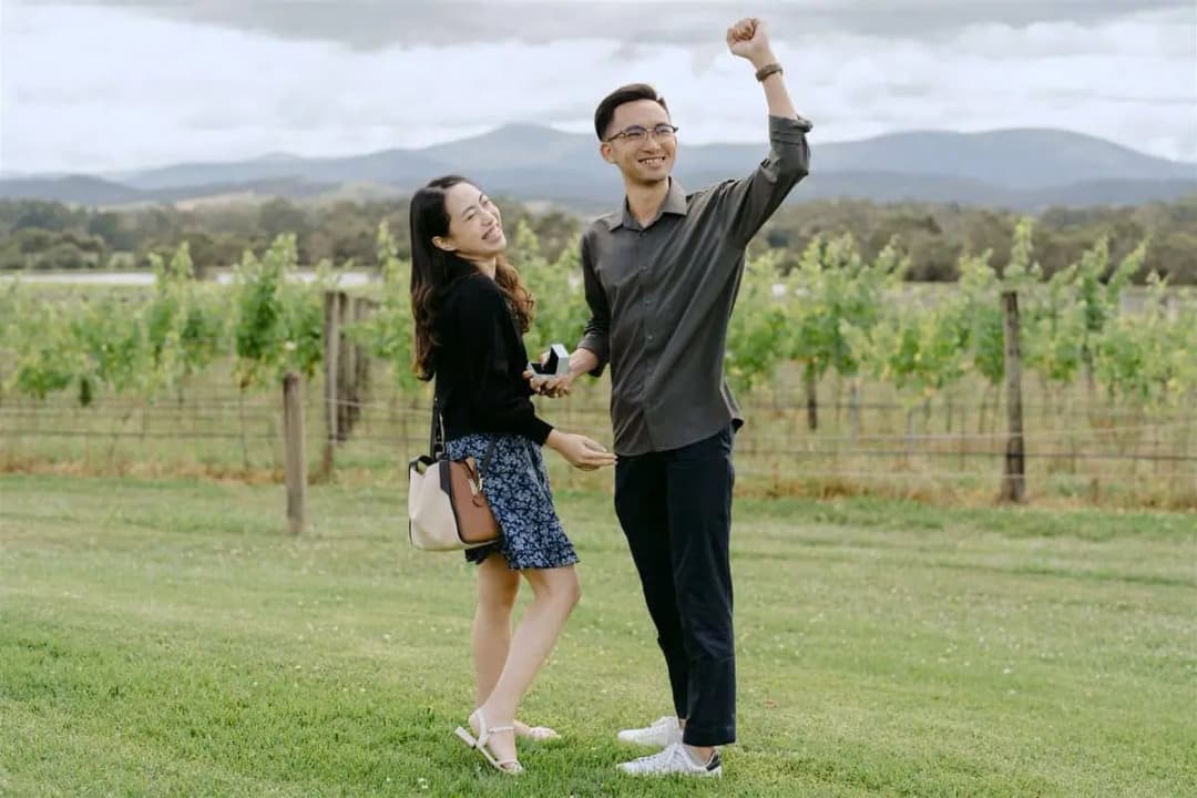 Couple smiling as the man raises a fist beside vineyard rows.