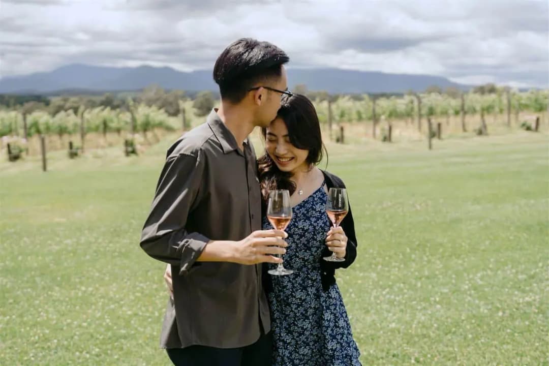 Couple embracing and holding sparkling wine glasses beside a vineyard.