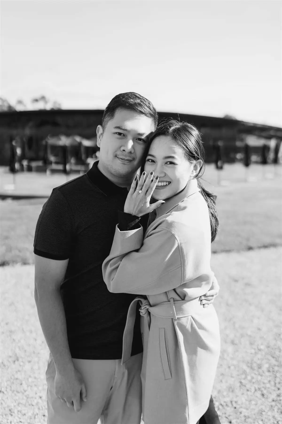 Black-and-white portrait of a smiling couple with the woman showing her ring.