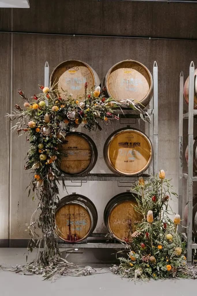 Floral ceremony display beside stacked wine barrels