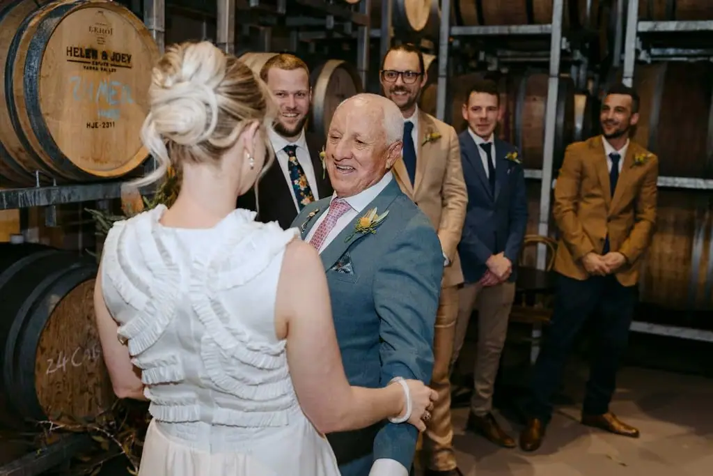 Bride greeting an older guest in front of wine barrels