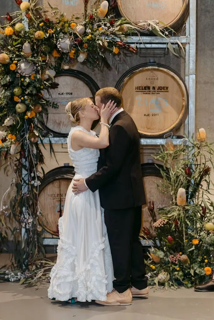 Couple kissing in front of stacked wine barrels