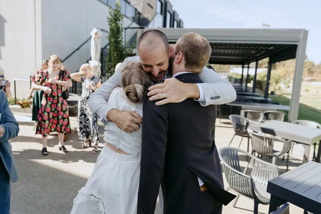 Couple embracing a wedding guest outside