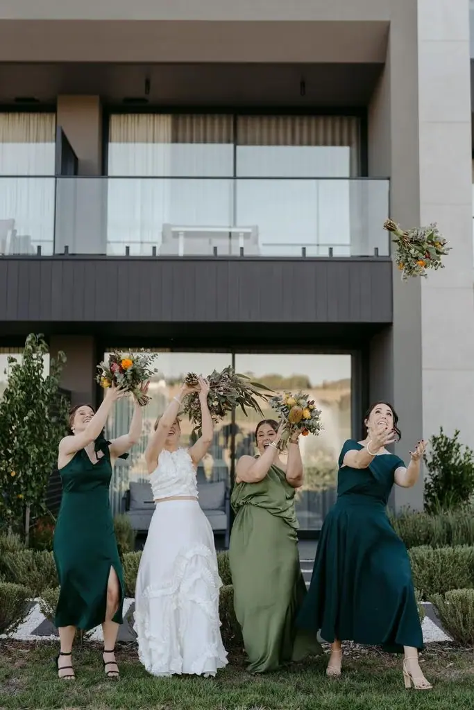 Bridesmaids lifting their bouquets outside the venue