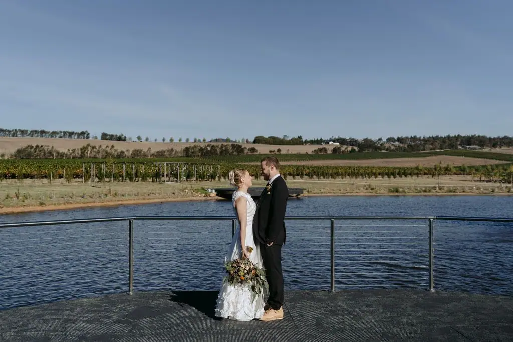 Couple standing on a lakeside jetty beside vineyard views
