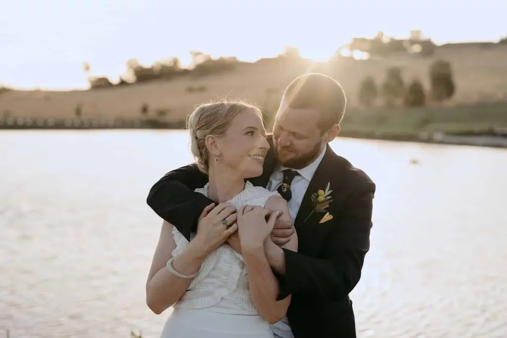 Bride kissing the groom's cheek beside the lake