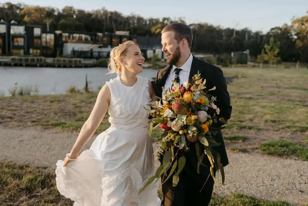 Couple walking beside the lake with the wedding venue behind them