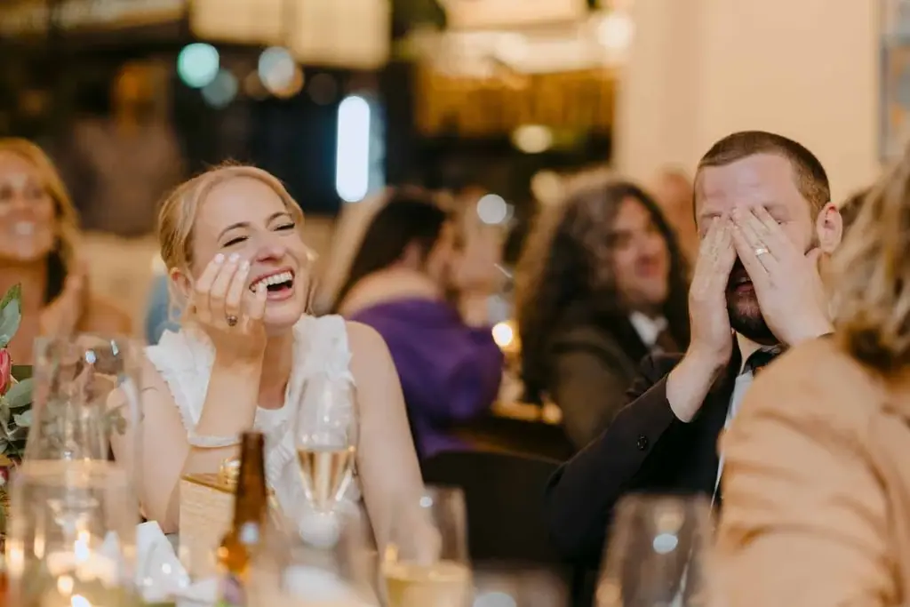 Seated newlyweds laughing and covering their mouths