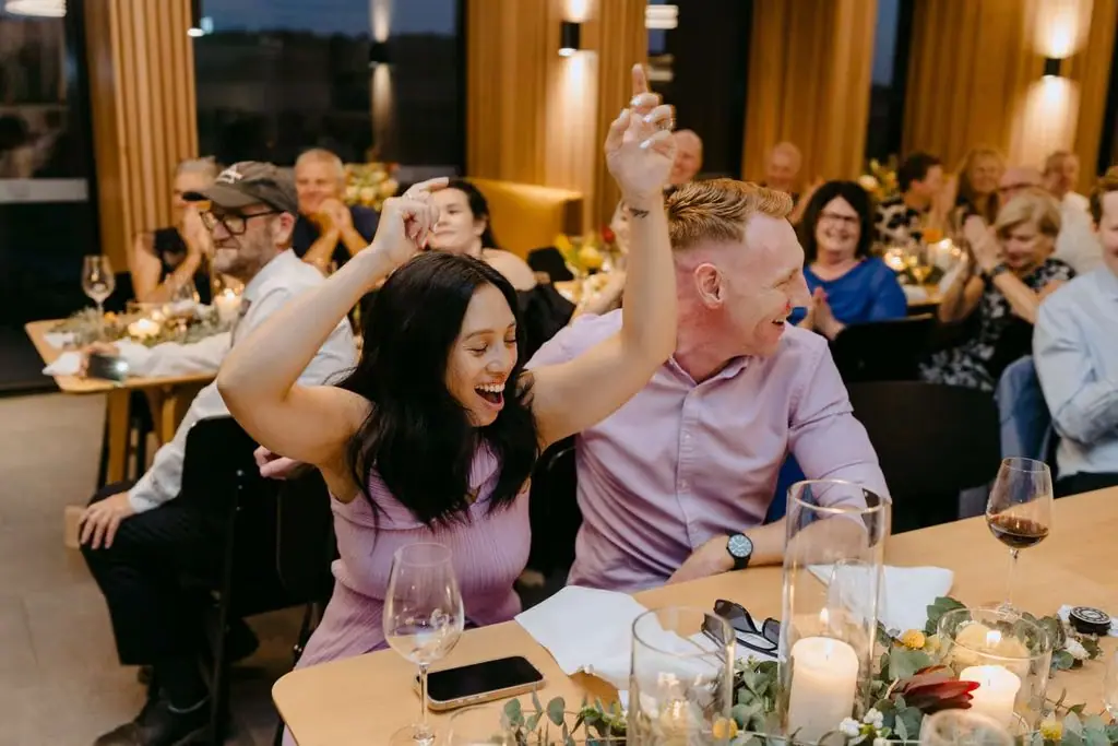 Two seated guests raising their arms at the reception