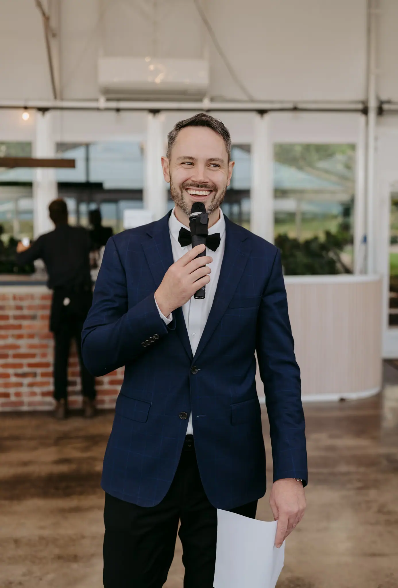 Man smiling and speaking into a microphone inside a marquee.