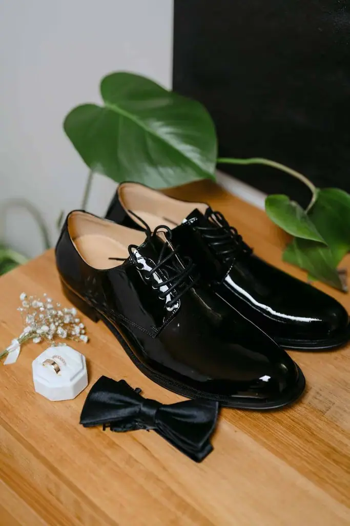 Black dress shoes, wedding accessories and a leaf on a timber table