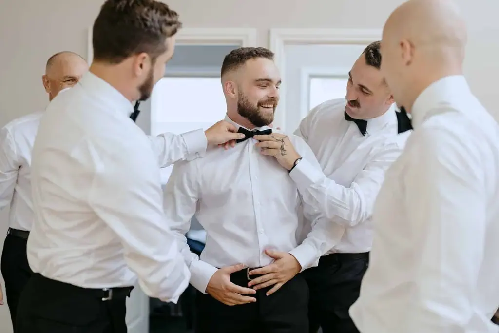 Groomsmen helping the groom fasten his bow tie