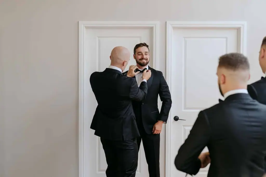Guest helping the groom fasten his bow tie