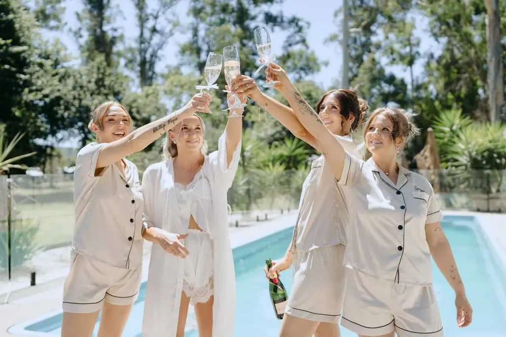 Bride and attendants raising their glasses by the pool