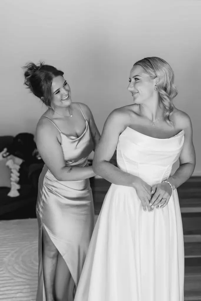 Black-and-white photograph of a guest helping the bride into her dress