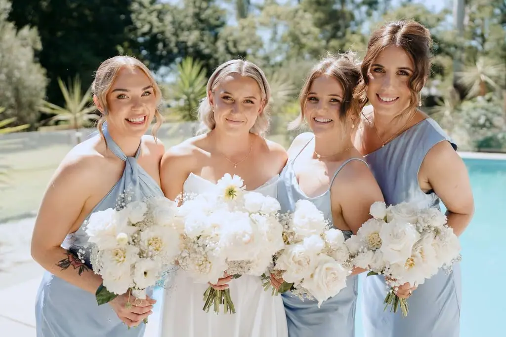 Bride and bridesmaids smiling with their white bouquets