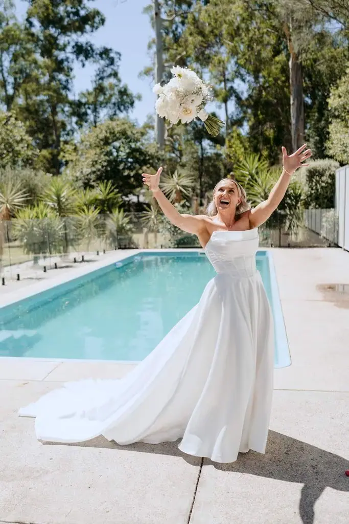 Bride raising her bouquet above her head beside the swimming pool