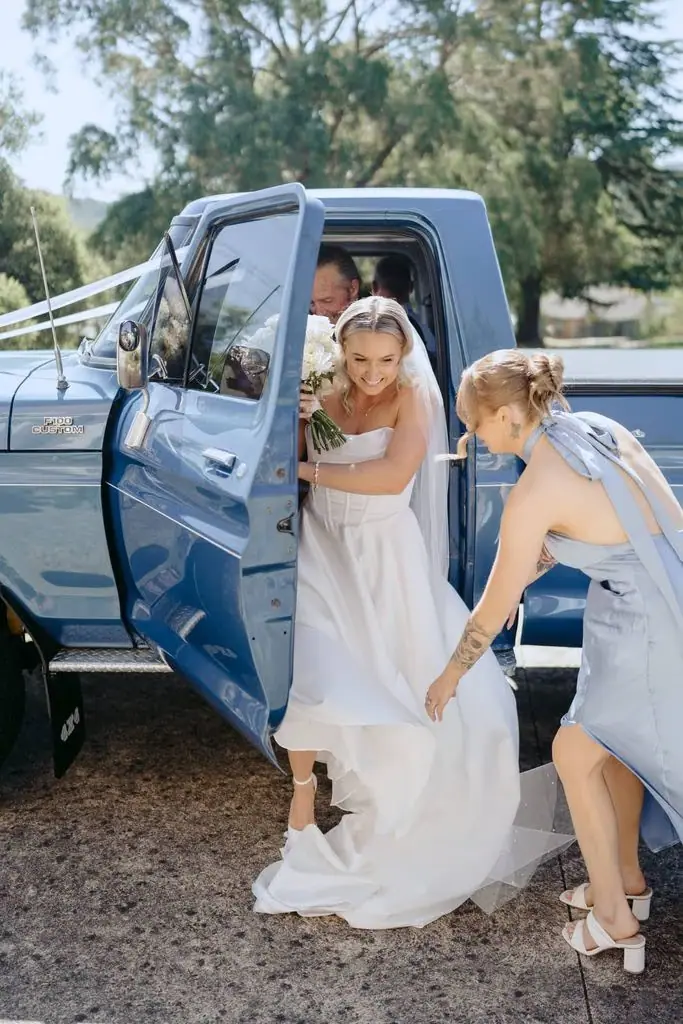 Bride stepping out of a vehicle with an attendant helping her dress