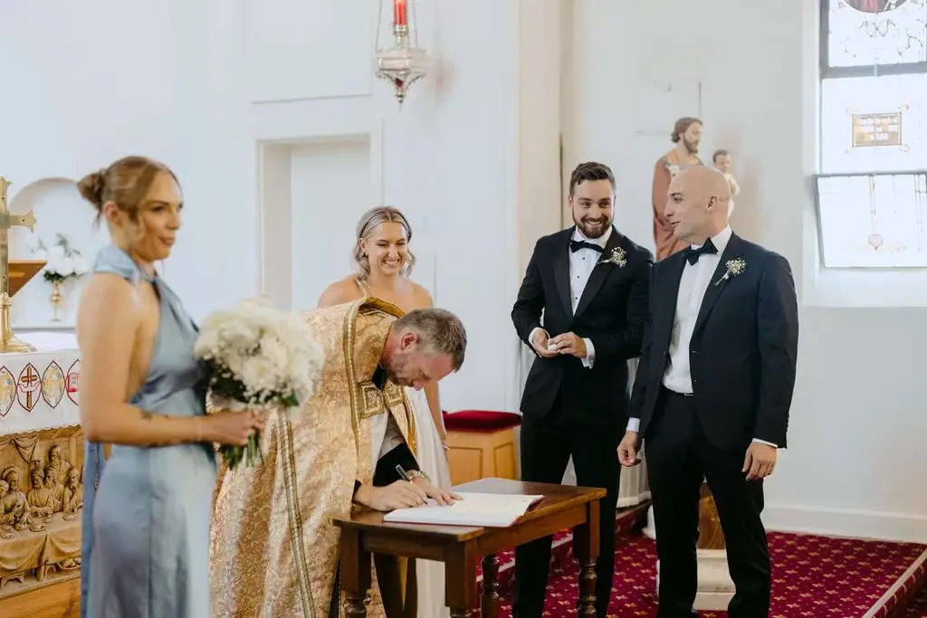 Guest signing the wedding register with the couple and another guest nearby