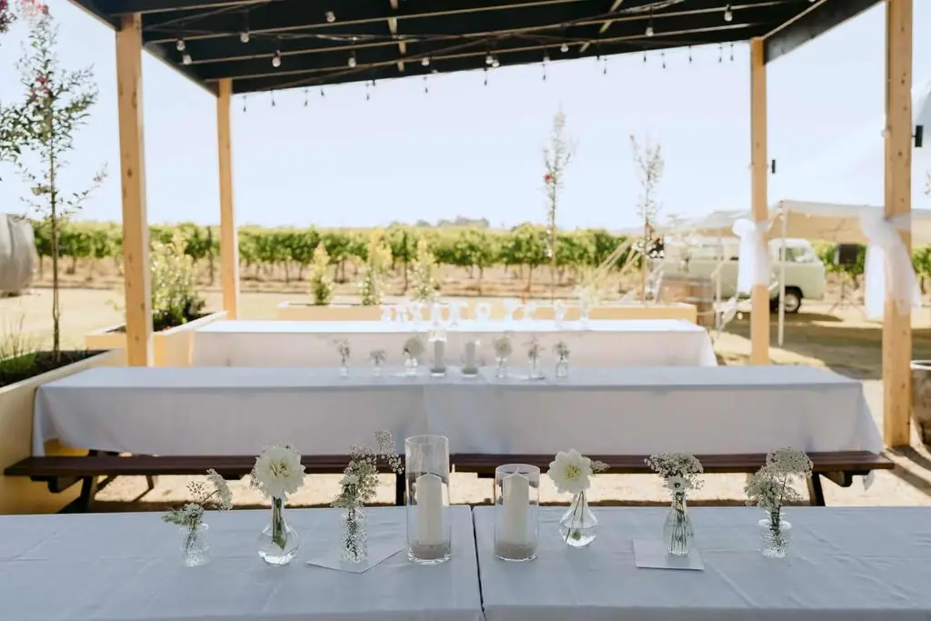 Rows of glasses on an outdoor reception table beneath a pergola