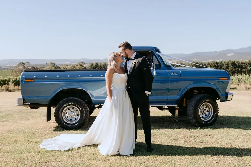 Couple kissing beside a blue pickup truck with hills behind them