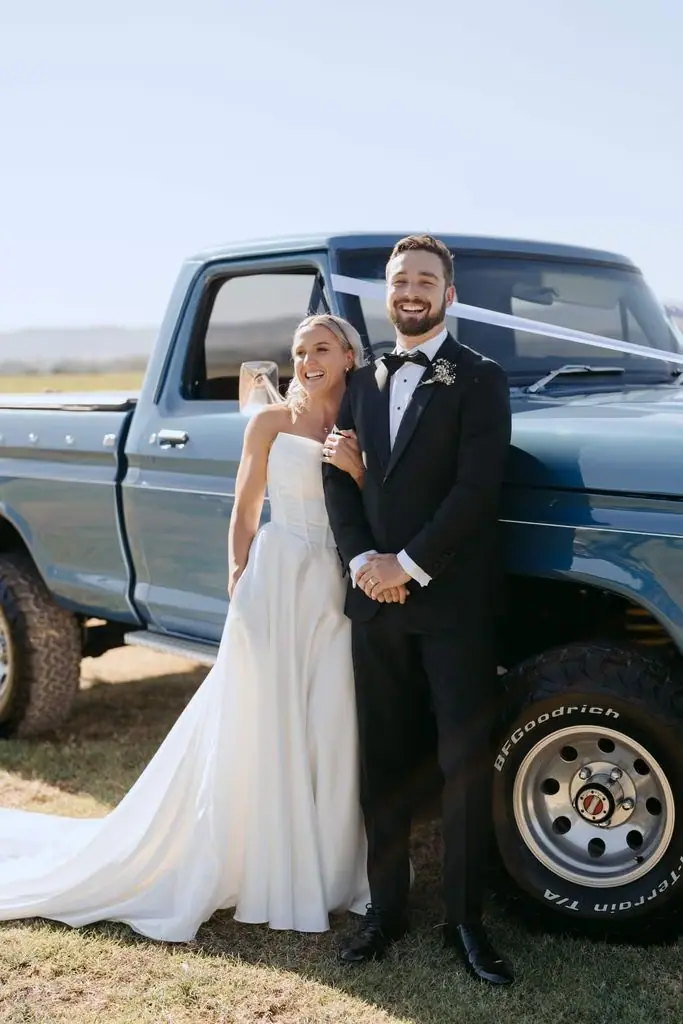 Couple posing beside the open door of a blue pickup truck