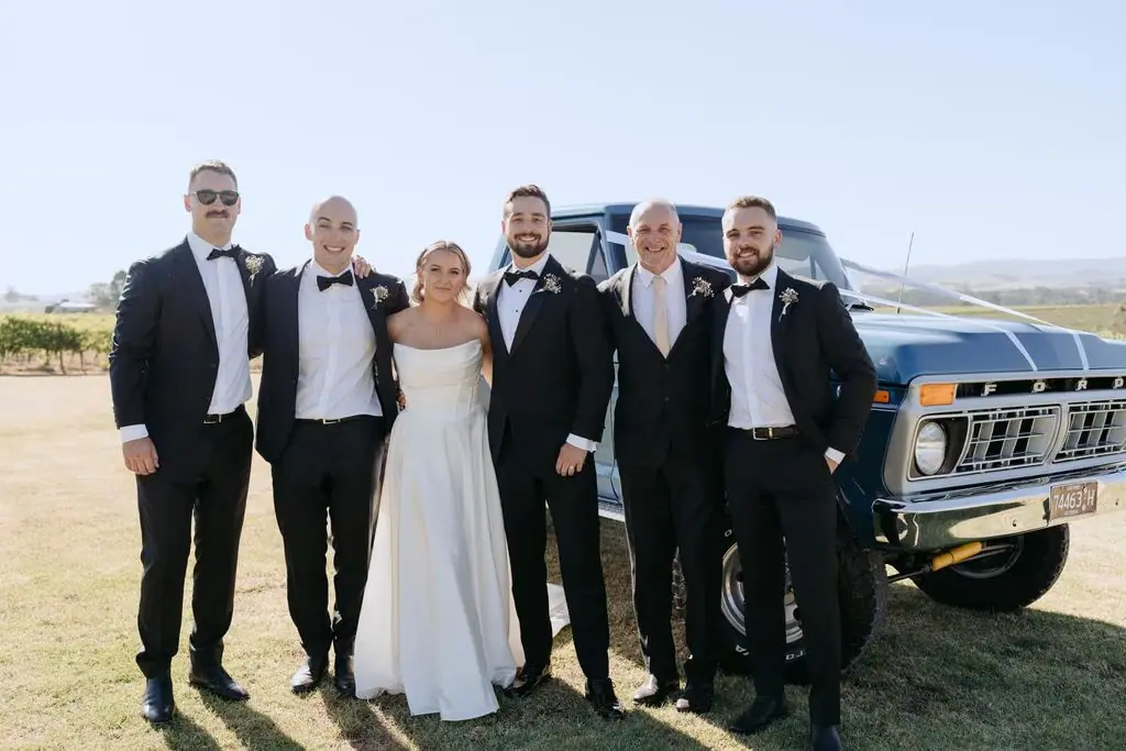 Wedding party standing together beside a blue pickup truck