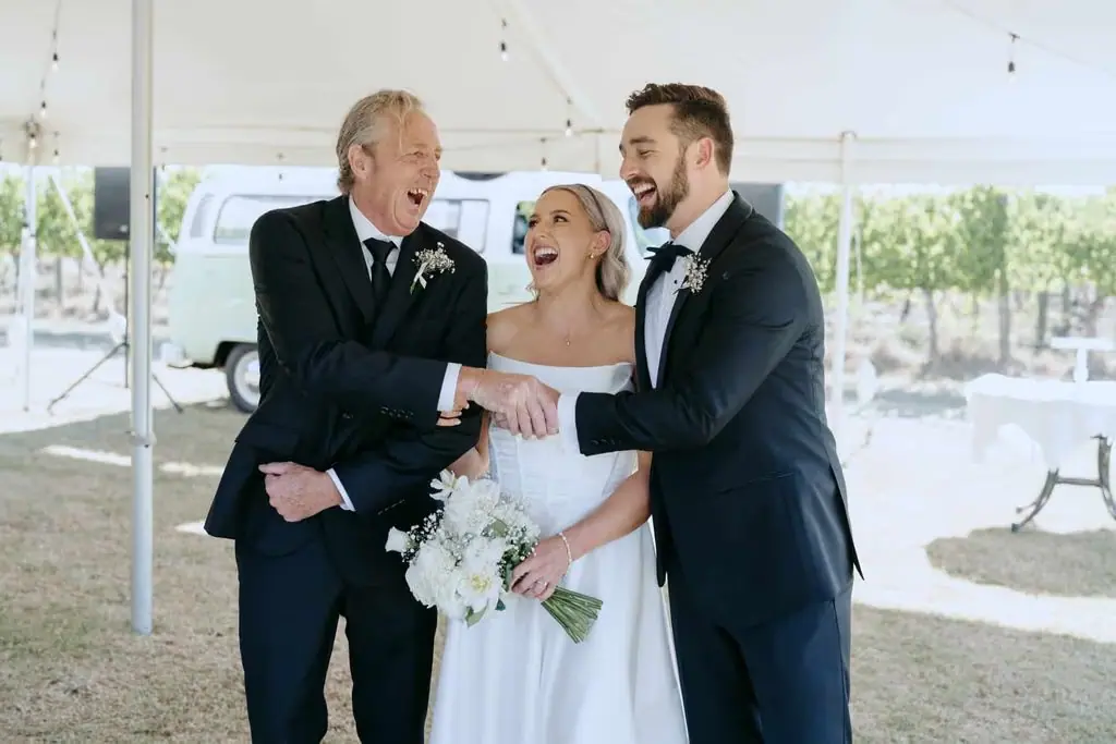Newlyweds laughing with an older guest beneath the reception marquee