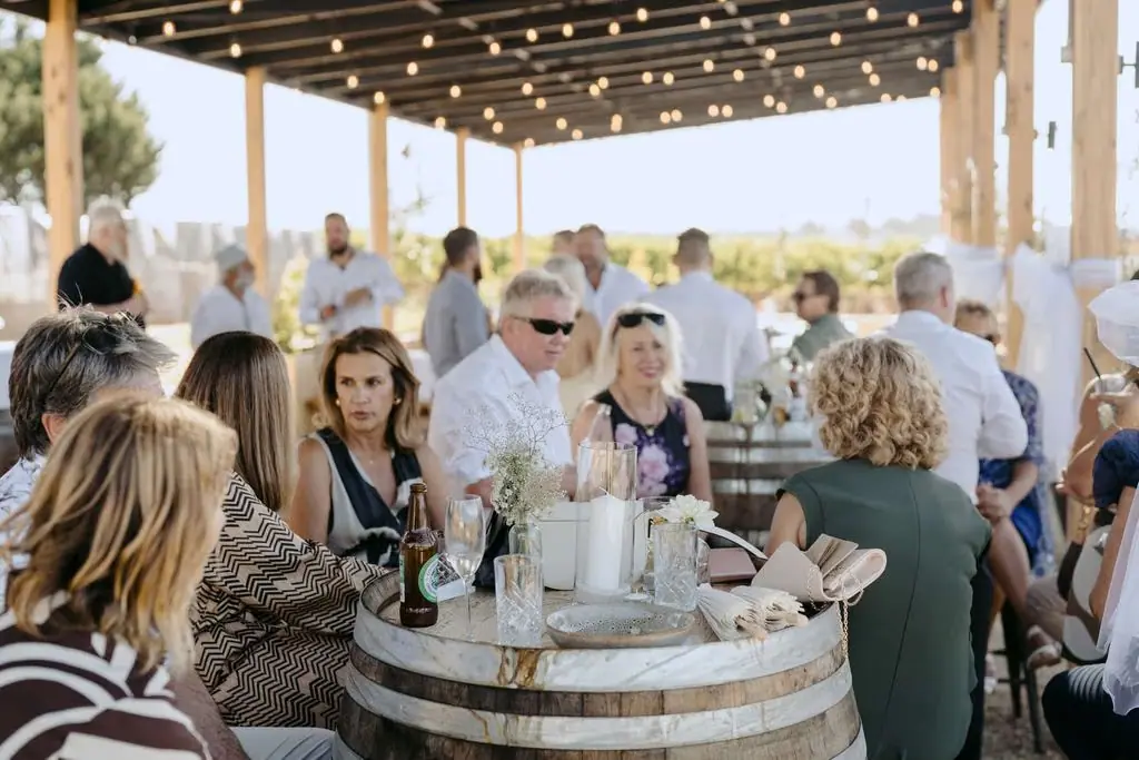 Guests chatting around a wine-barrel table beneath string lights