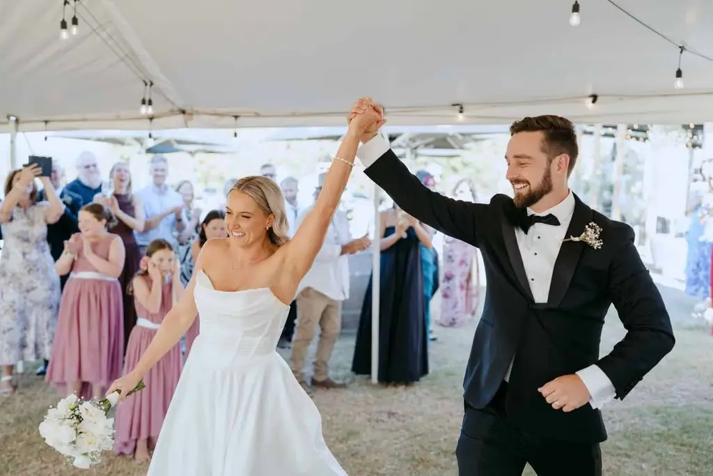 Groom holding up the bride's hand as guests watch beneath the marquee