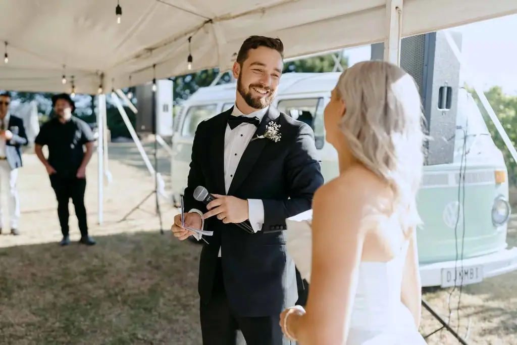 Groom smiling at the bride while holding a microphone
