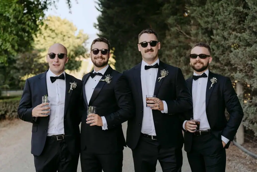 Groom and groomsmen wearing sunglasses and holding drinks outdoors