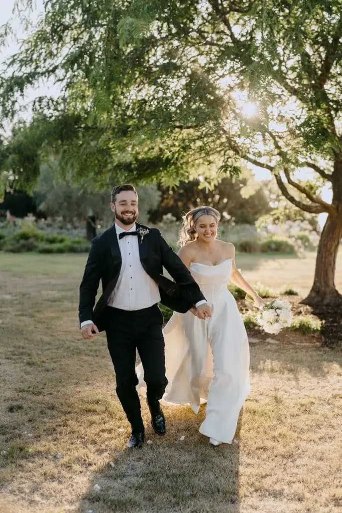 Couple holding hands and walking beneath leafy trees