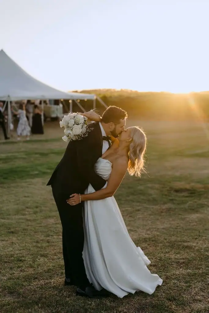 Couple embracing in a field beside the marquee at sunset
