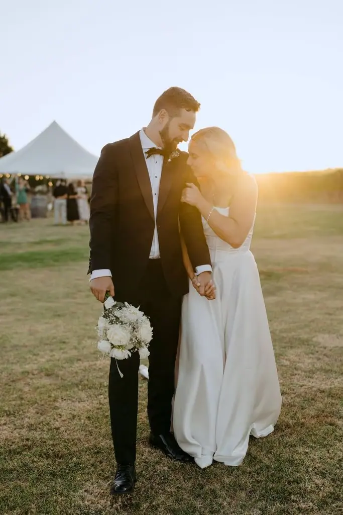 Couple standing close together beside the marquee at sunset