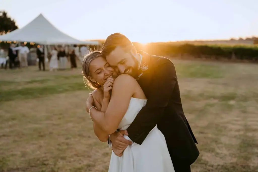 Groom embracing the bride from behind beside the marquee