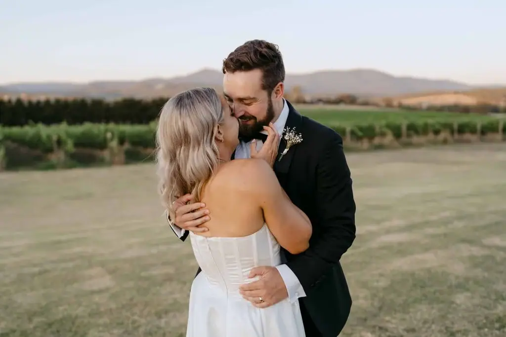 Groom kissing the bride's head with vineyard hills behind them
