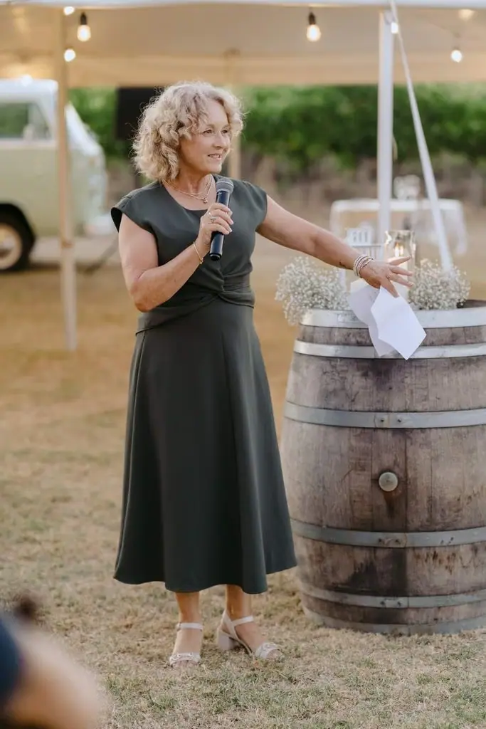 Guest speaking into a microphone beside a wine-barrel table