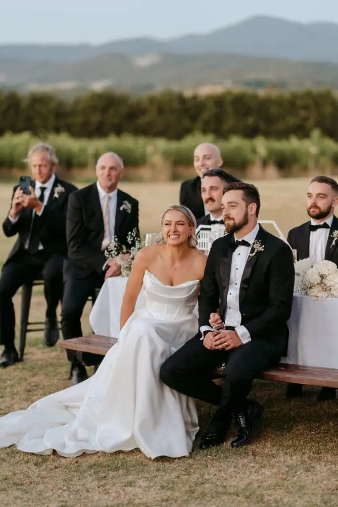 Newlyweds seated together as guests watch the speeches