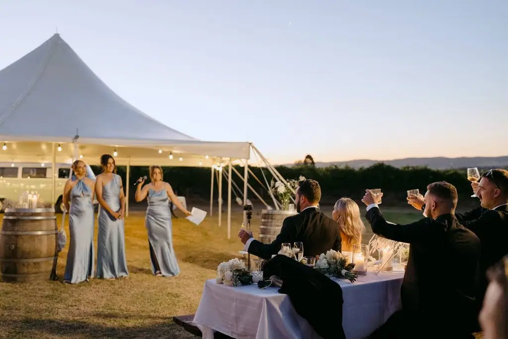 Bridesmaids speaking to guests beside the marquee at dusk