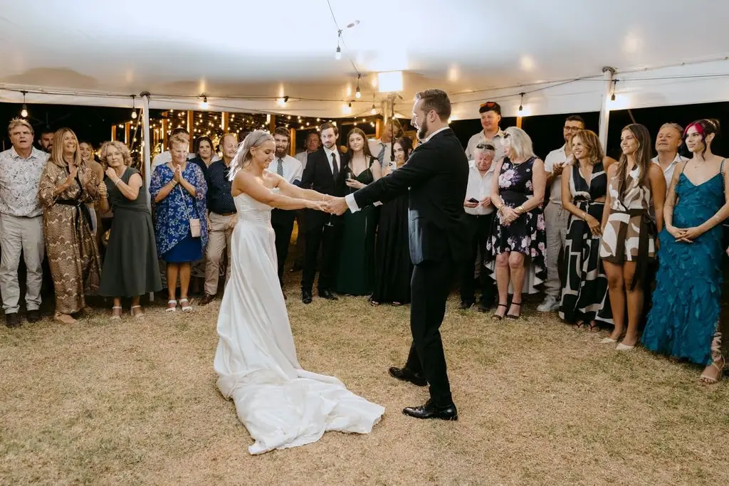 Newlyweds holding hands during their first dance as guests watch