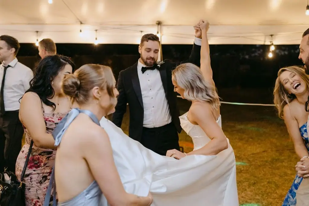 Guests holding the bride's skirt as she dances beside the groom