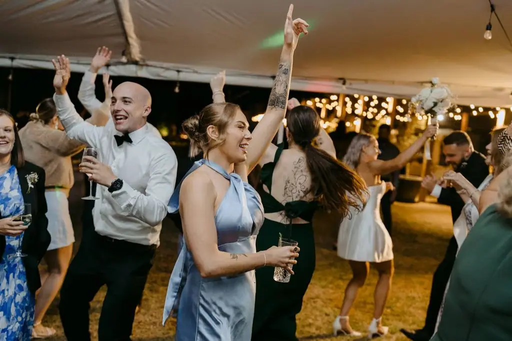 Guests raising their arms and dancing together beneath the marquee