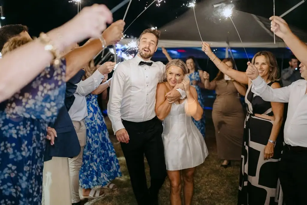 Newlyweds walking beneath sparklers held by their guests