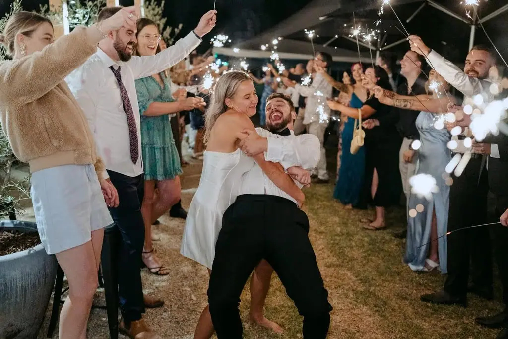 Groom leaning back and carrying the bride through a sparkler farewell